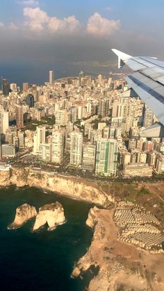 an airplane wing flying over a large city next to the ocean with buildings on both sides