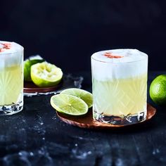 two glasses filled with lemonade and limes on top of a black countertop