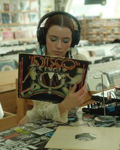 a woman sitting at a table with headphones on and reading a book in front of her