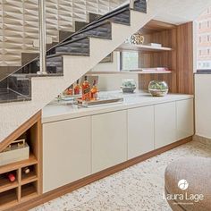 a kitchen with white cabinets under a stair case and wine bottles on the counter top