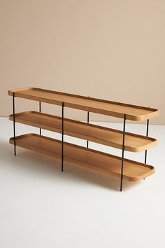 three tiered wooden shelf with black metal legs on white floor, in front of beige wall