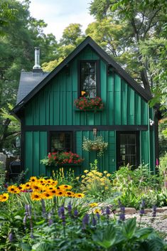 a green house with lots of flowers in the front yard and windows on each side