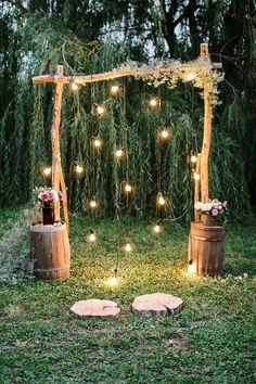 an outdoor ceremony with wooden barrels and string lights on the grass, surrounded by greenery