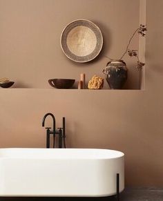 a bath tub sitting next to a brown wall in front of a shelf with vases on it