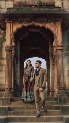 a man and woman standing on steps in front of an old building with stone pillars