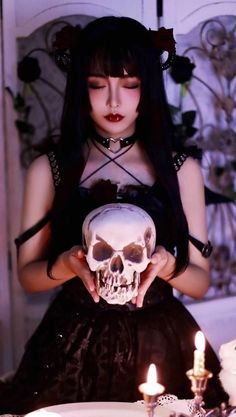 a woman holding a skull in front of a table with candles and other items on it