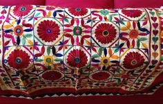 a red couch covered in colorfully embroidered fabric on top of it's back