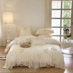 a white bed sitting in a bedroom next to a window with curtains on the windowsill