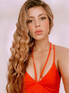 a woman with long curly hair wearing an orange top