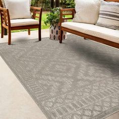 an outdoor area with two wooden chairs and a gray rug on the ground next to a couch