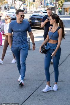 a man and woman are walking down the street with other people in the back ground