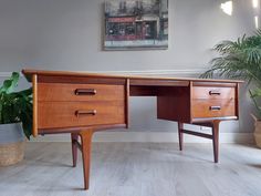 a wooden desk with two drawers and a potted plant on the floor next to it