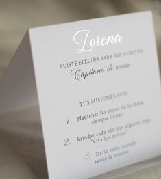 a close up of a menu card on a white table cloth with silver foil lettering