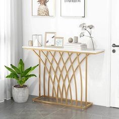 a white and gold console table with two pictures on the wall above it next to a potted plant