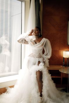 a woman in a white dress standing next to a window