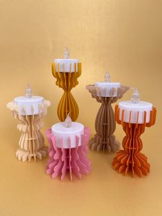 four different colored candles sitting next to each other on a yellow surface with one candle in the middle