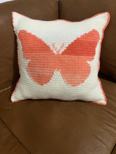 an orange and white butterfly pillow on a brown couch