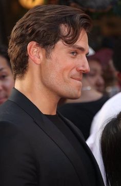 a close up of a person wearing a suit and smiling at the camera with people in the background