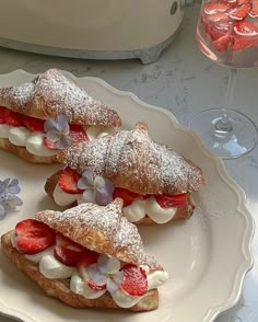 three pastries with strawberries and whipped cream are on a plate next to a glass of wine