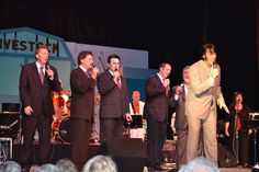 a group of men standing on top of a stage next to each other holding microphones