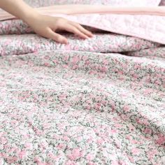 a person is laying in bed with pink and green flowers on the comforter cover