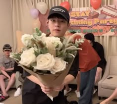 a young man holding a bouquet of flowers in his hands while people sit on the couch behind him