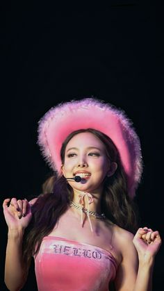 a young woman wearing a pink outfit and hat with her hands in the air while smiling