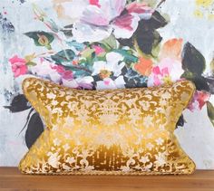 a gold pillow sitting on top of a wooden table next to a floral wallpaper