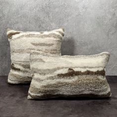 two brown and white pillows sitting next to each other on a wooden table in front of a concrete wall