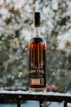 a bottle of whiskey sitting on top of a wooden table next to snow covered trees