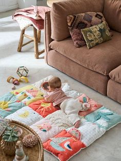 a baby laying on top of a blanket in front of a couch with pillows and toys