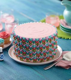 a colorful cake sitting on top of a table next to cupcakes and saucers