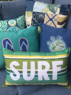 several pillows on a blue couch with the word surf printed on them and flip flops