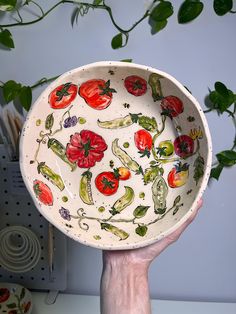 a hand holding up a bowl with tomatoes and peppers painted on the inside of it