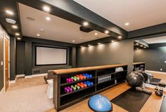 a home gym with an exercise ball on the floor and a large screen in the background