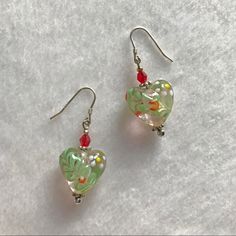 two heart shaped glass beads are hanging from silver earwires on a white surface