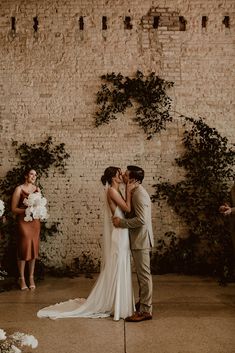 a bride and groom kissing in front of an ivy covered wall at their wedding ceremony