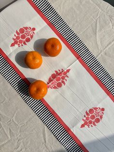 three oranges sitting on top of a white and red table cloth next to each other