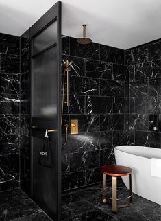 a bathroom with black marble walls and flooring, including a white bathtub next to a walk in shower