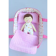 a doll in a pink and white bag with polka dots on the bottom, next to a blanket