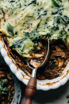 a white bowl filled with mushroom and spinach casserole next to a spoon