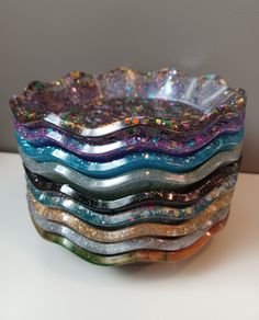 a stack of multicolored glass bowls sitting on top of a white table next to a wall