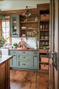 an open kitchen with wooden floors and green cabinetry, along with lots of greenery