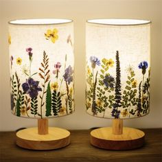 two lamps with floral designs on them sitting on a wooden stand next to each other