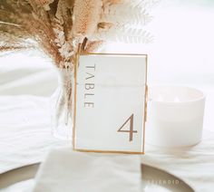 the table numbers are displayed in front of a vase with dried flowers and a candle