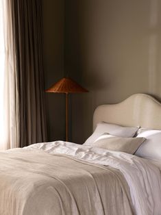 a bed sitting next to a window in a bedroom under a large lamp on top of a table