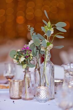 three vases filled with flowers on top of a white table cloth covered tablecloth