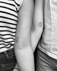 two people standing next to each other with tattoos on their arms