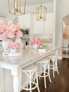 pink flowers are in white vases on the kitchen island