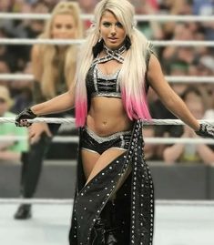 a woman with pink hair standing in front of a wrestling ring wearing black and silver clothing